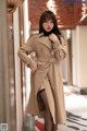 A woman in a beige trench coat is posing for a picture.