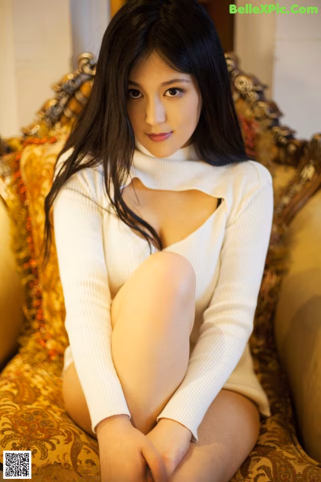 A woman sitting on a couch in a white sweater.