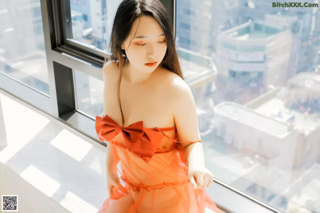 A woman in an orange dress sitting on a window sill.
