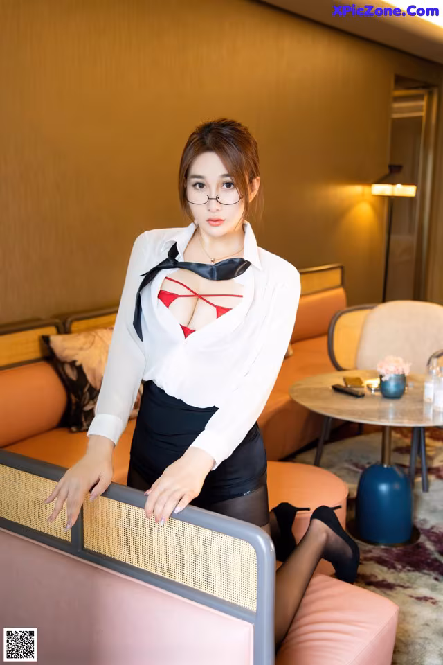 A woman in a white shirt and black skirt posing on a couch.