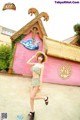 A woman in a bikini and straw hat posing in front of a pink building.