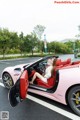 A woman sitting in the driver's seat of a pink sports car.