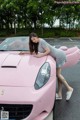 A woman leaning on the hood of a pink sports car.