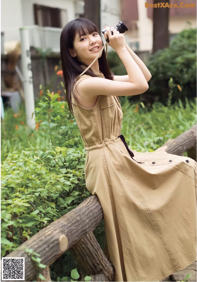 A woman in a beige dress holding a camera.