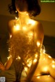 A naked woman sitting on a bed covered in lights.