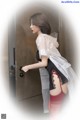 A woman in a white shirt and black skirt is opening a door.