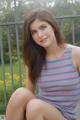 A young woman sitting on a wooden bench in a striped tank top.