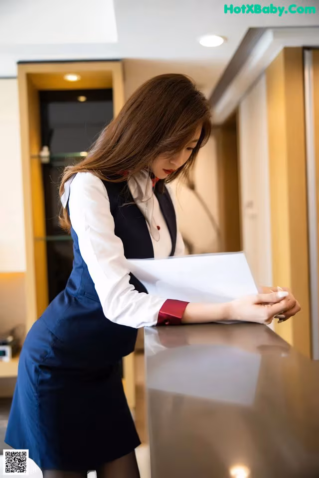 A woman in a blue dress is looking at a piece of paper.